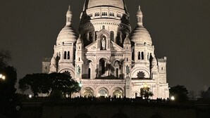 Een grote, verlichte kathedraal met meerdere koepels en beelden, met ingewikkelde architectonische details en een opvallende centrale koepel.