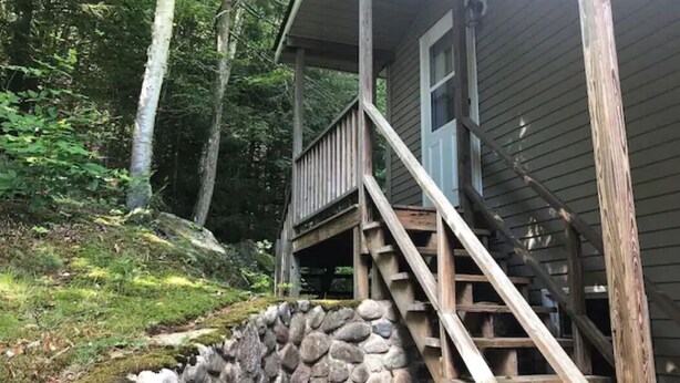 A cabin with a stone retaining wall, wooden stairs, and a porch.