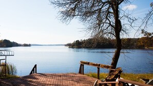 Una terraza de madera con barandilla que da a un lago tranquilo, rodeada de árboles y zonas verdes.