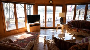 Una sala de estar con muebles de mimbre, un televisor y ventanas amplias con vistas a una terraza.