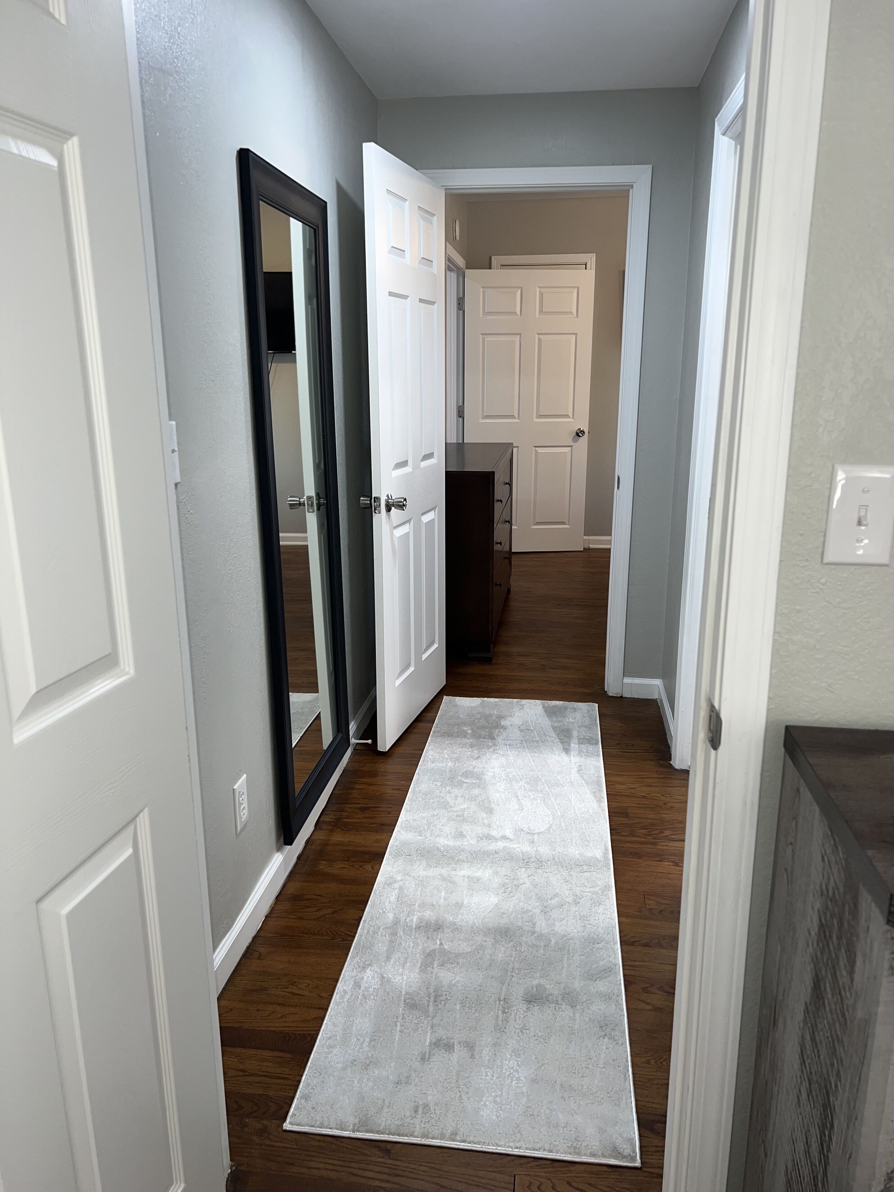A hallway with white doors, a dark wooden floor, and a grey rug.