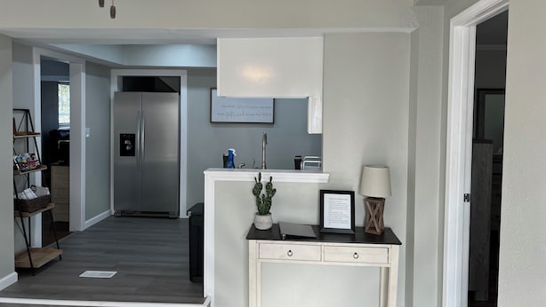 A modern kitchen with a stainless steel refrigerator, a built-in oven, and a white countertop. There is a ceiling fan with lights, a small potted plant, and a framed sign on the wall. - Entire beautiful home w/ great location!  (Paducah)