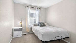 A bedroom with a single bed, a nightstand, a lamp, and a window with blinds.