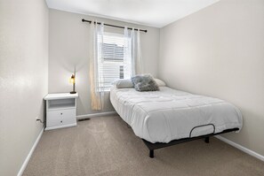 A bedroom with a single bed, a nightstand, a lamp, and a window with blinds.