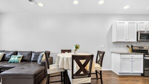 A modern kitchen with white cabinets, a stainless steel oven, and a dining area with a round table and chairs. - Modern 3BR Furnished Home Near DIA with 2-Car Garage (Denver)