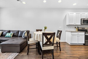 A modern kitchen with white cabinets, a stainless steel oven, and a dining area with a round table and chairs. - Modern 3BR Furnished Home Near DIA with 2-Car Garage (Denver)