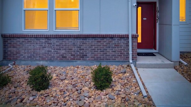 A two-story residential building with a red door, multiple windows, and a stone foundation. - Modern 3BR Furnished Home Near DIA with 2-Car Garage (Denver)