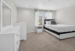 A bedroom with a bed, bedside tables, a dresser, and a window with curtains. - Modern 3BR Furnished Home Near DIA with 2-Car Garage (Denver)