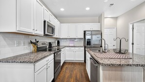 A modern kitchen with white cabinets, granite countertops, stainless steel appliances, and a wooden floor. - Modern 3BR Furnished Home Near DIA with 2-Car Garage (Denver)