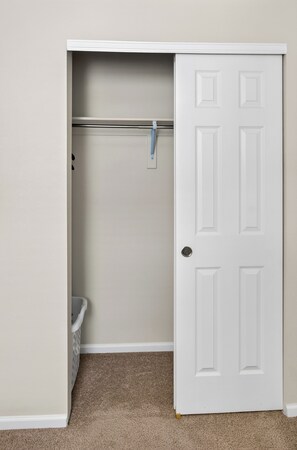 A closet with a hanging rod, a door, and a trash bin.