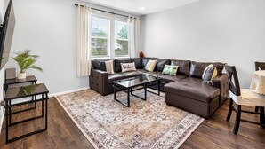 A modern living room with a sectional sofa, a glass coffee table, and a patterned rug.