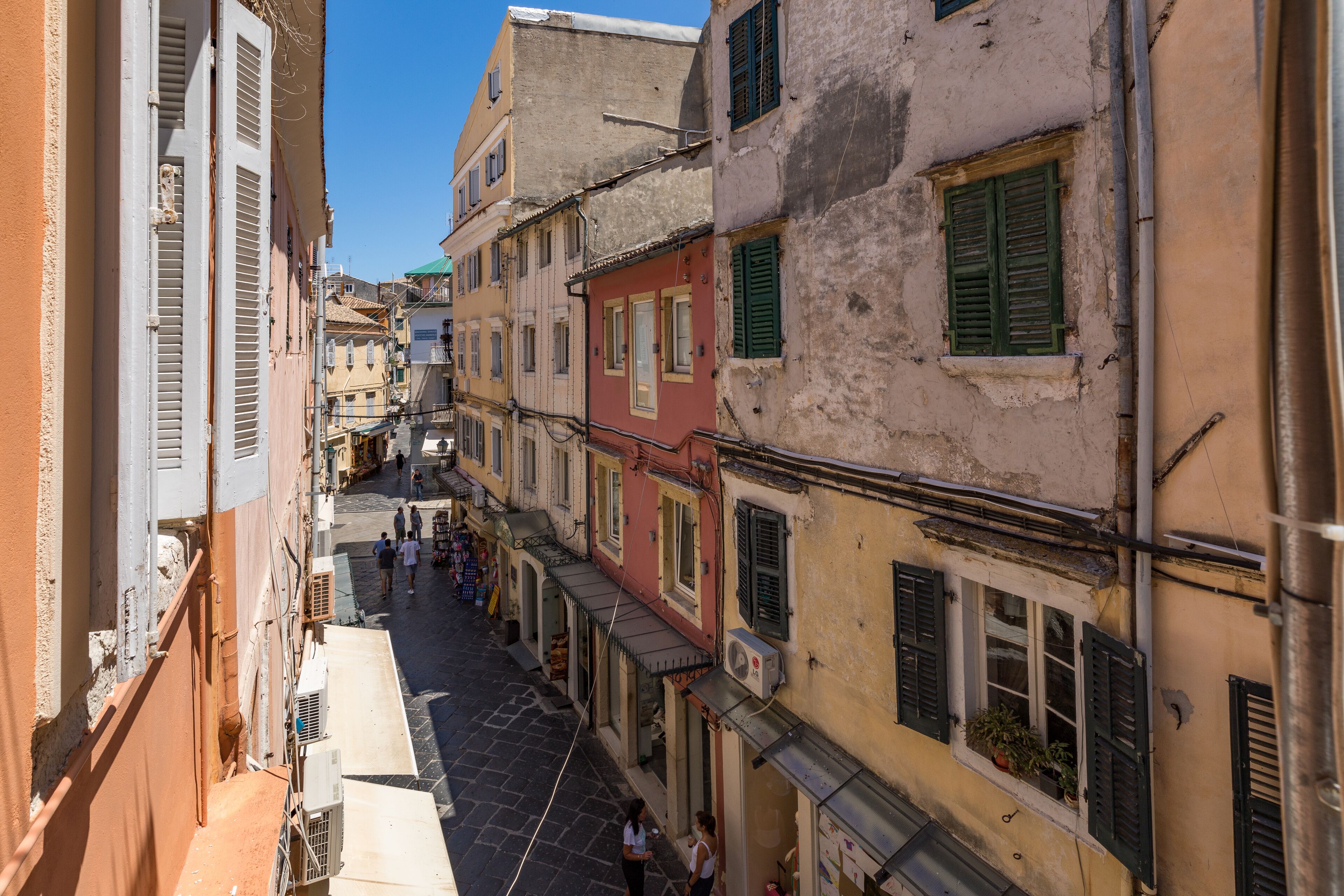 Une rue étroite, bordée de bâtiments des deux côtés, avec des balcons et des volets.