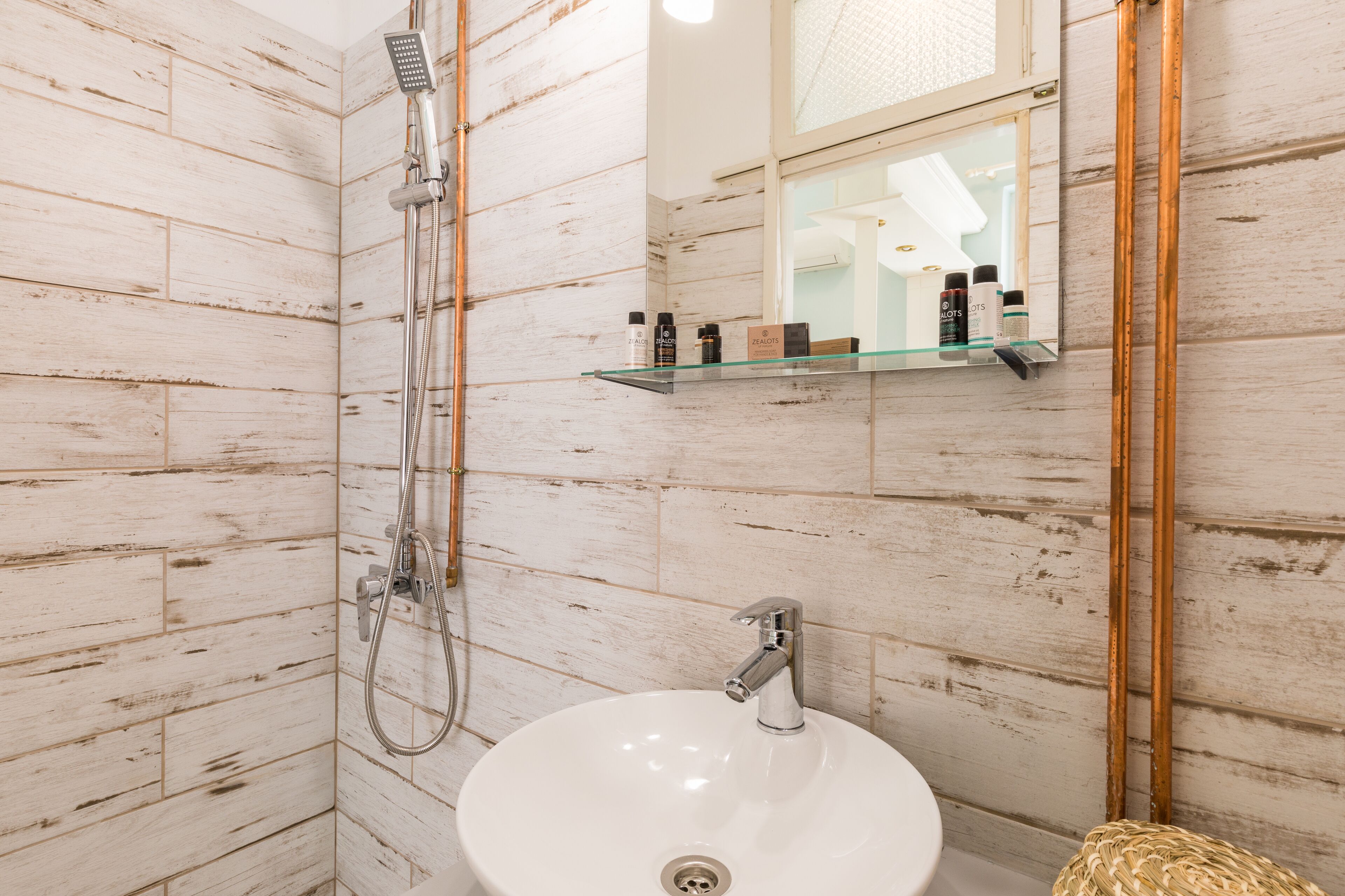 A bathroom with a white sink, a handheld showerhead, and a mirror with a shelf above it.