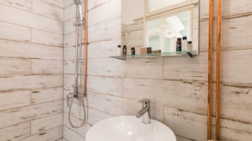 A bathroom with a white sink, a handheld showerhead, and a mirror with a shelf above it.