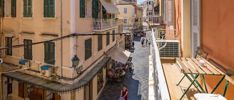 A narrow street with buildings on both sides, outdoor seating, and a few people walking.