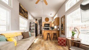 Una cocina moderna con armarios de madera, una isla central con taburetes y un comedor con un otomano estampado rojo.