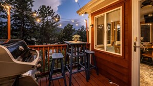 Una terraza de madera con una parrilla, asientos al aire libre y luces colgantes.