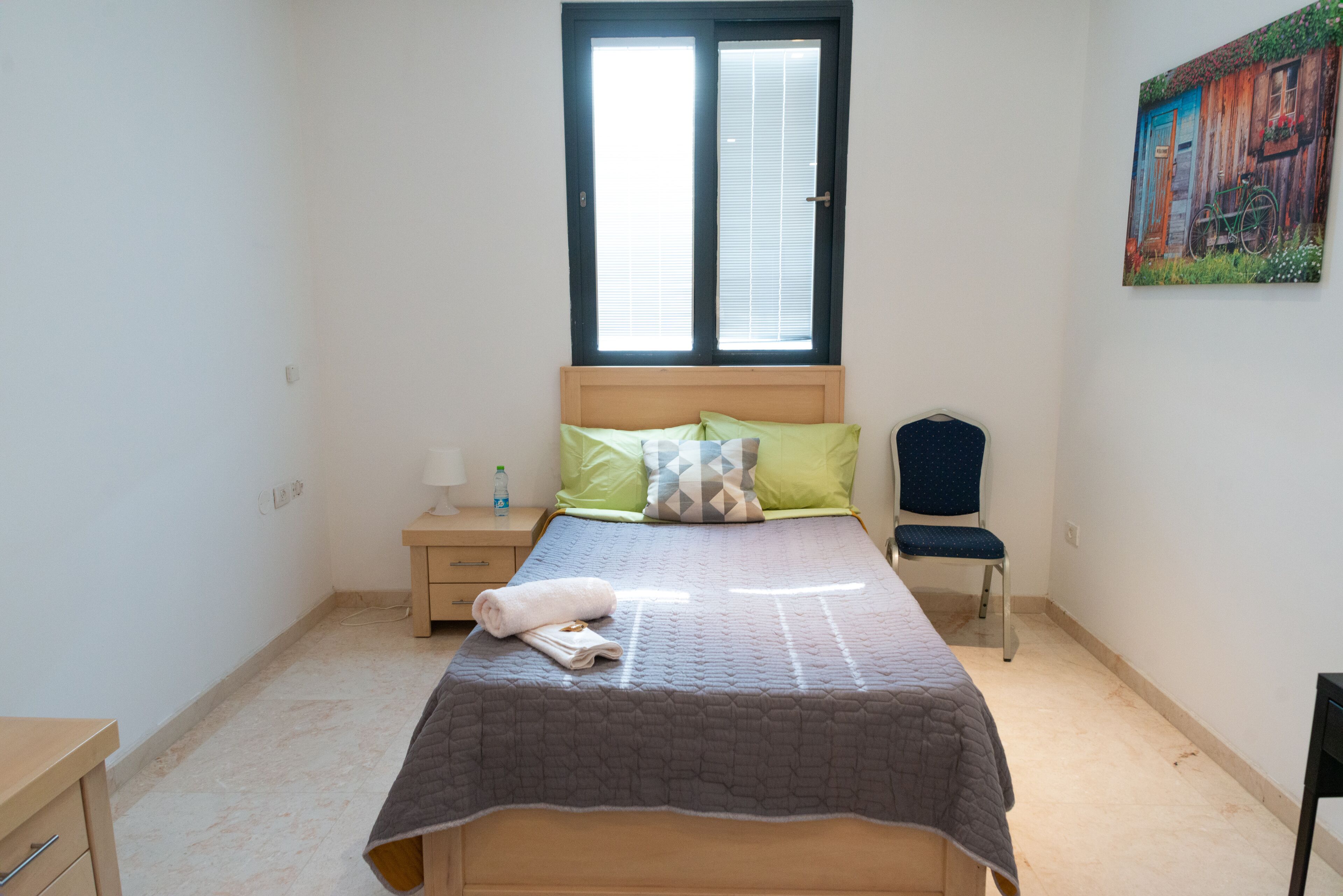 A bedroom with a bed, a chair, a nightstand, and a window.