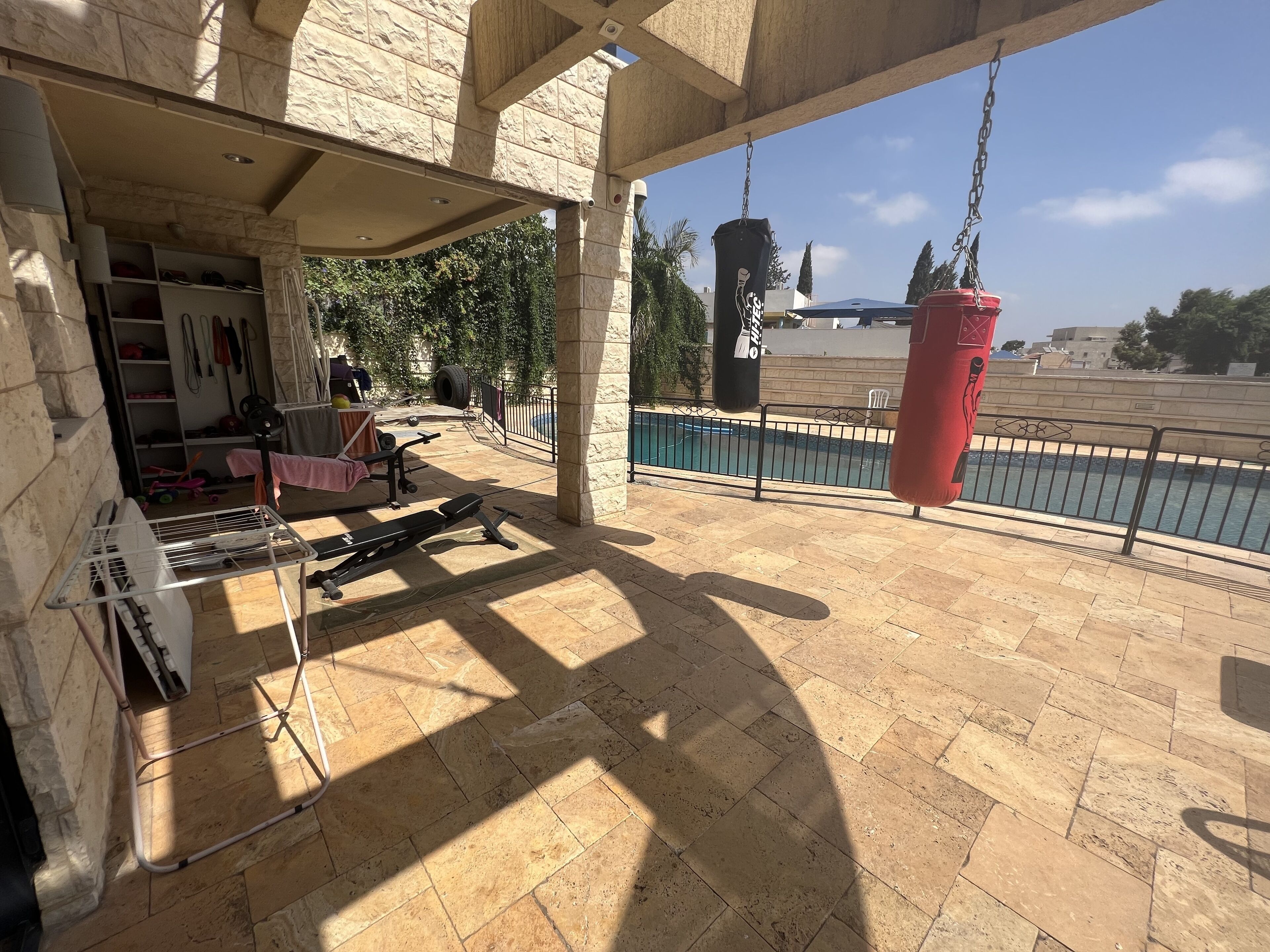 A covered outdoor area with exercise equipment, a pool, and a stone wall.