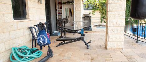 An outdoor gym area with exercise equipment, a water hose, and a bag on the ground.