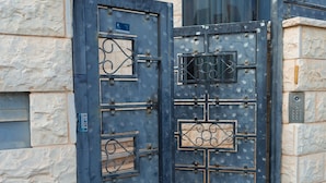 A set of ornate metal gates with intricate designs, leading to a building with stone walls and a large cylindrical structure in the background. - Grace Holon Villa & Pool (Holon)