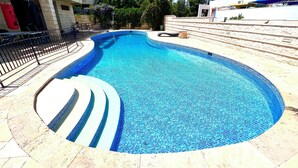 A swimming pool with a curved design, surrounded by stone steps and a metal fence. - Grace Holon Villa & Pool (Holon)