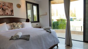 A neatly made bed with pillows and a rolled towel, a large window with a view of greenery, and a door to an outdoor area. - Grace Holon Villa & Pool (Holon)