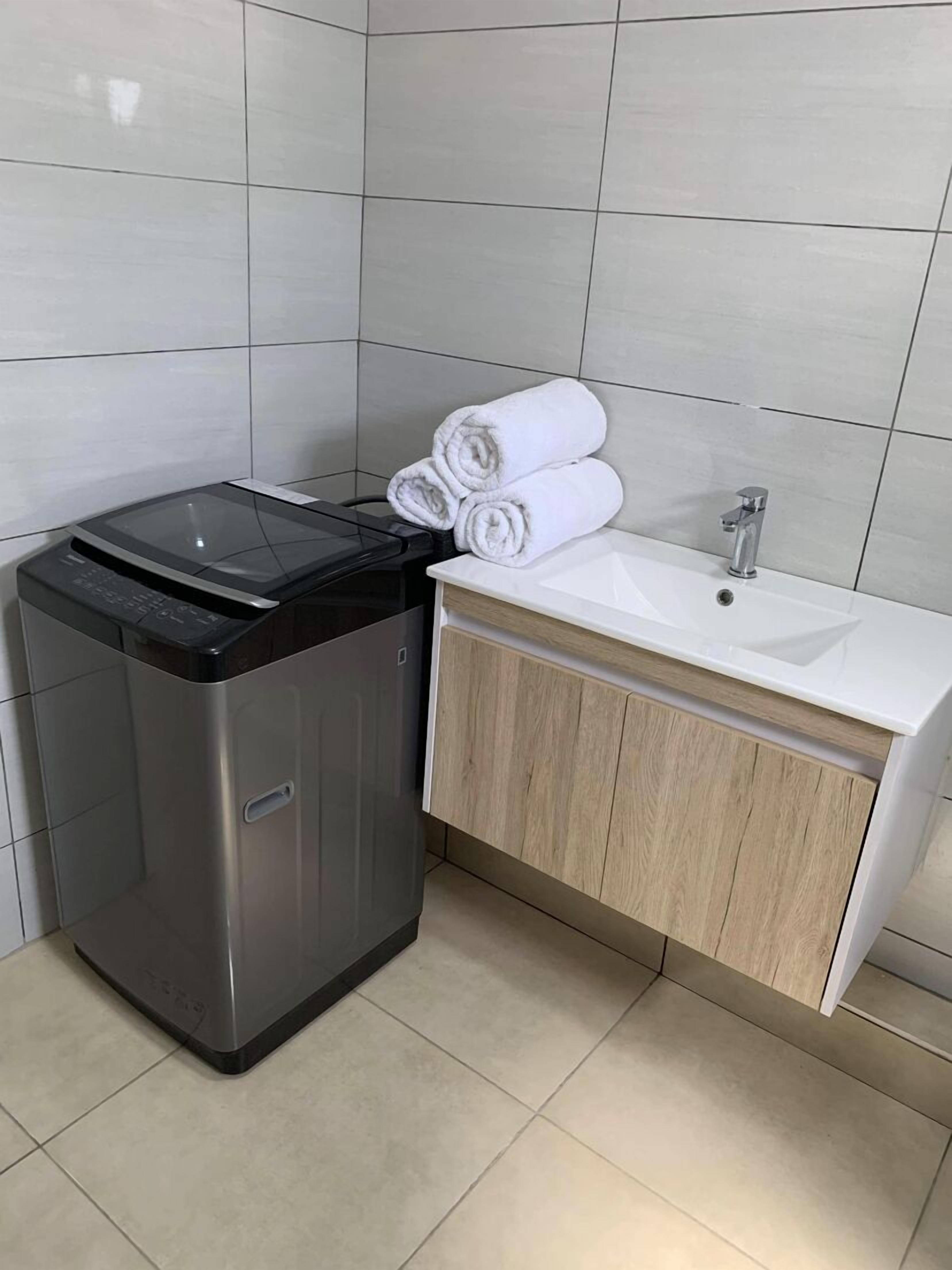 A compact, modern bathroom with a built-in washing machine, a sink, and neatly folded towels.