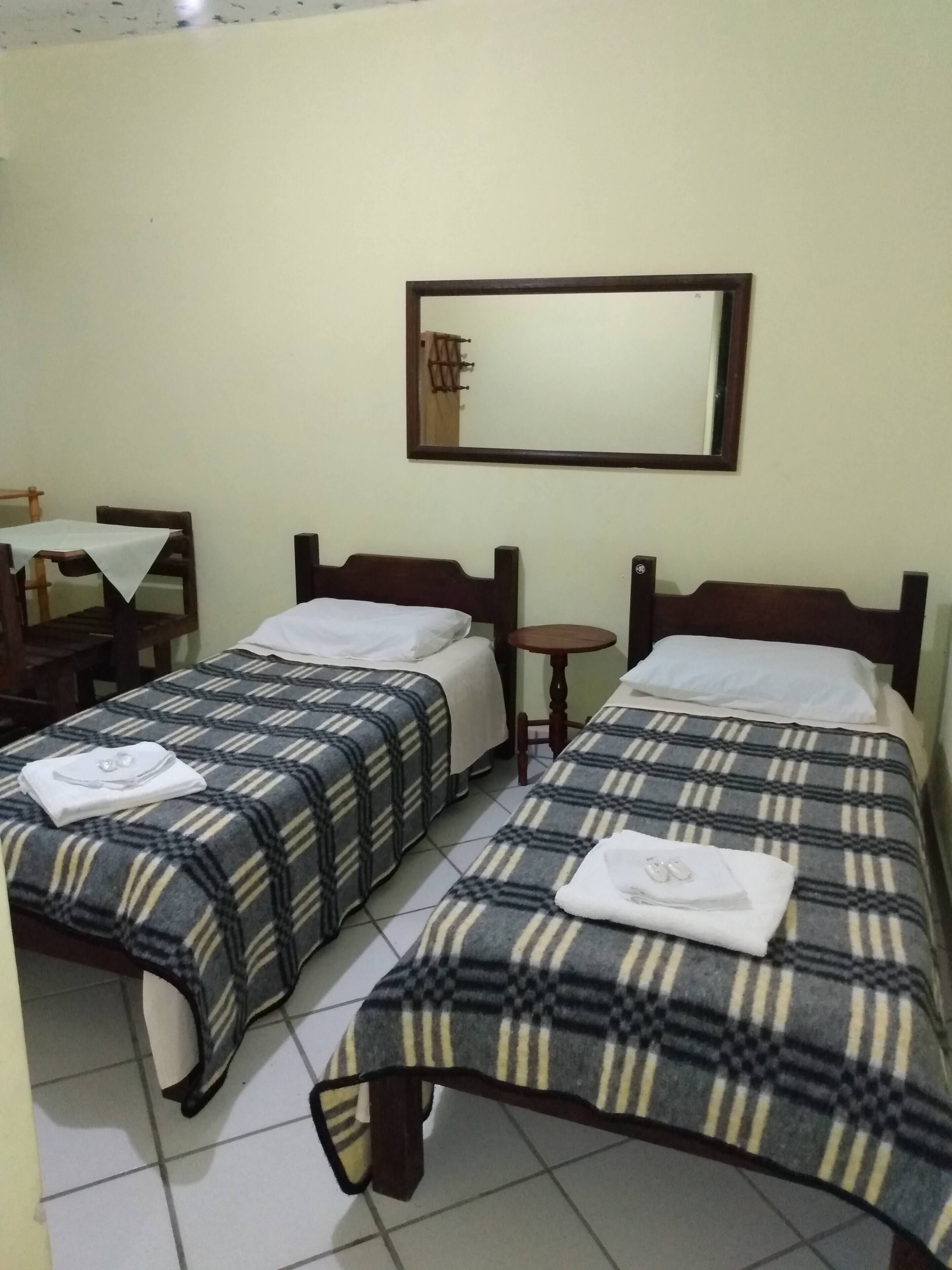 A hotel room with two single beds, a small table, and a chair.