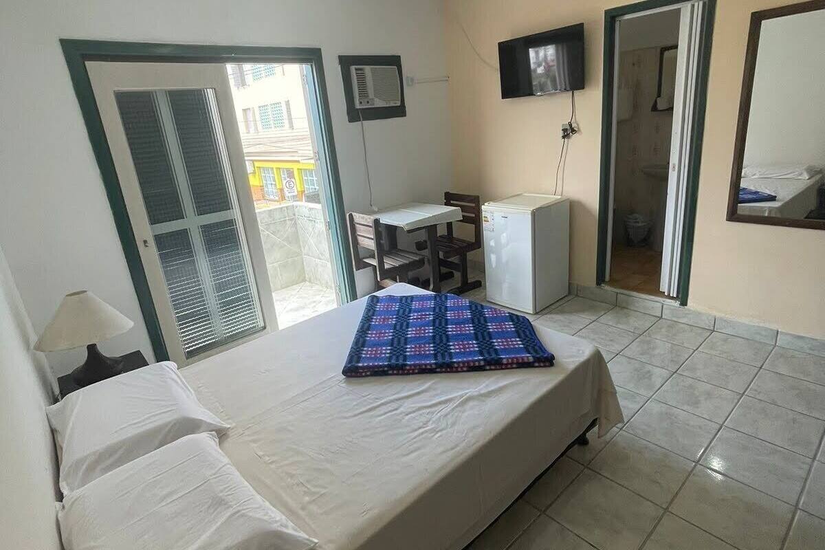 A bedroom with a bed, a desk, a TV, and a bathroom visible through an open door.