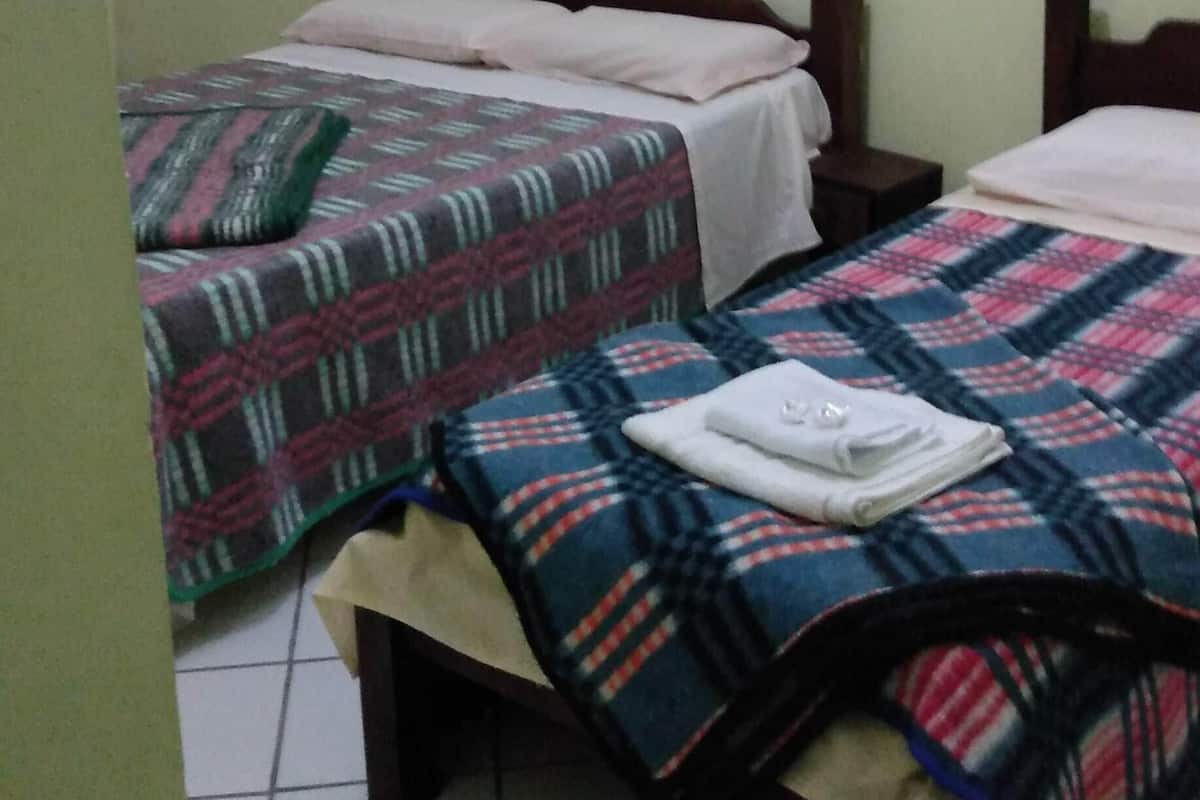 A small, simple room with two beds, each with a patterned blanket, a wooden headboard, and a plain wall.