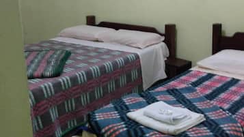 A small, simple room with two beds, each with a patterned blanket, a wooden headboard, and a plain wall.