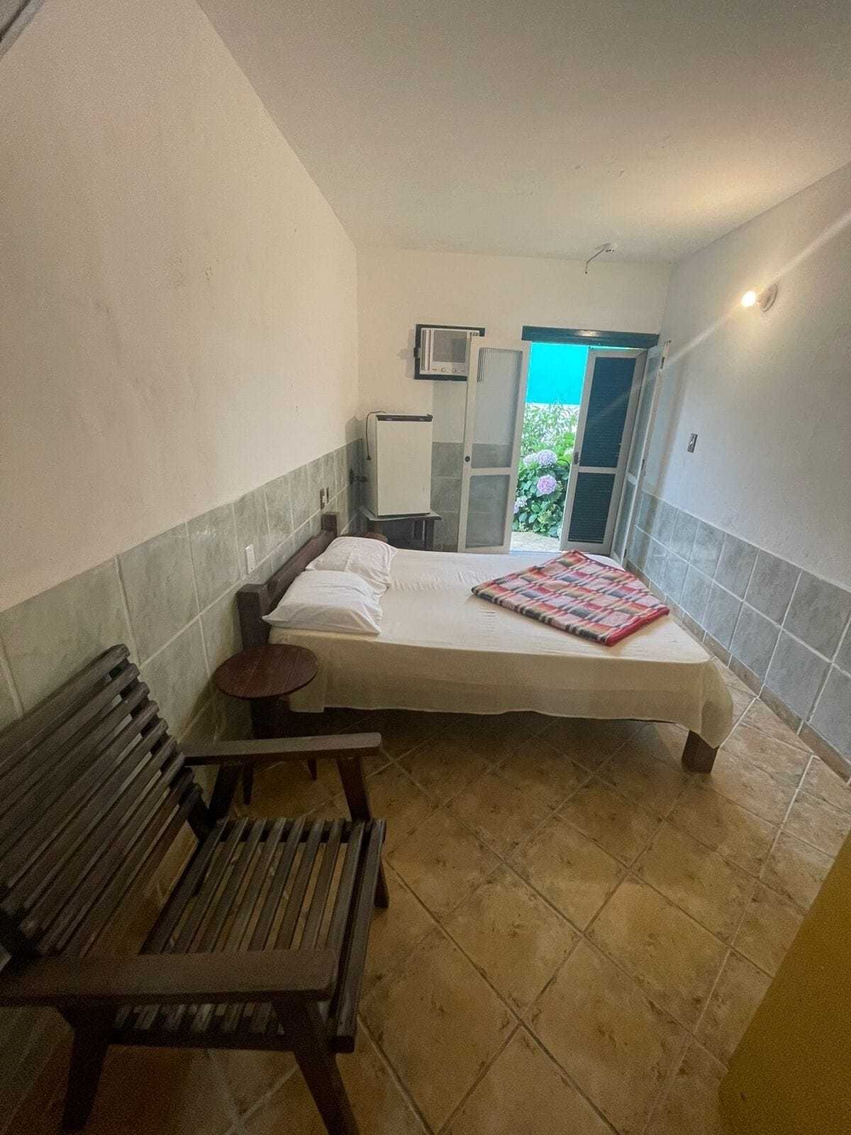 A bedroom with a bed, a bench, a small table, a microwave, and a door leading to a balcony.