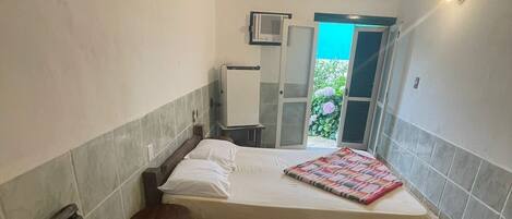 A bedroom with a bed, a bench, a small table, a microwave, and a door leading to a balcony.