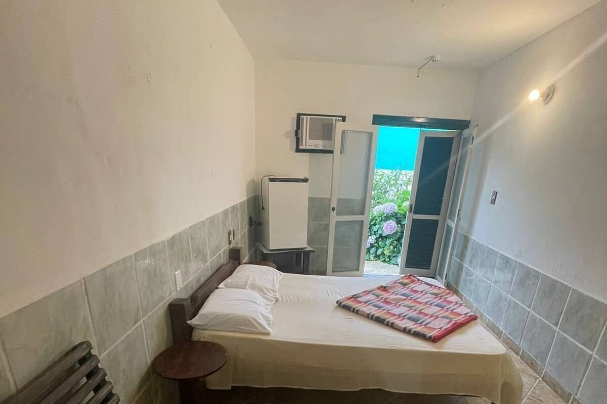 A bedroom with a bed, a bench, a small table, a microwave, and a door leading to a balcony.