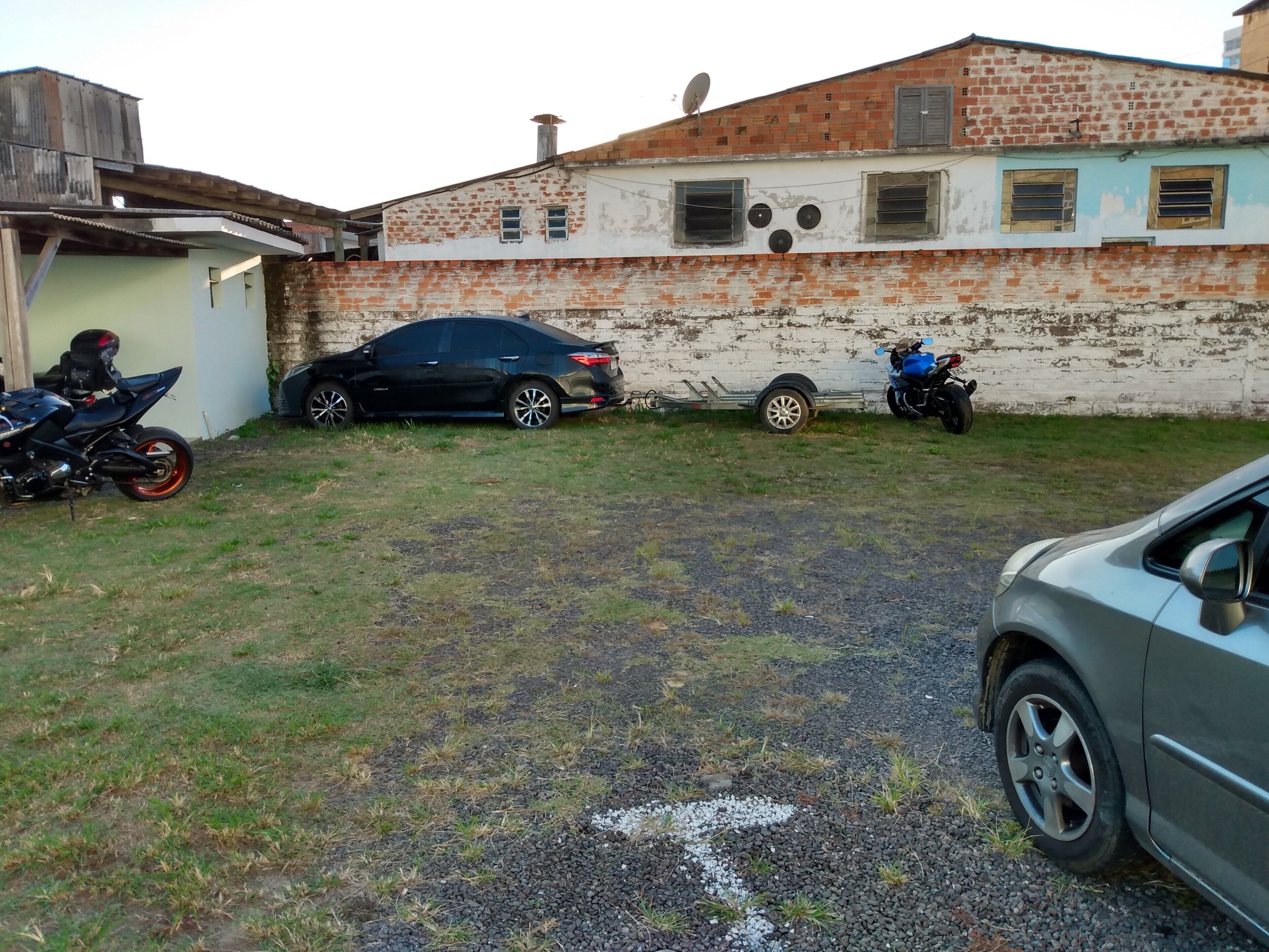 Un barrio residencial con un edificio de ladrillo, un coche negro, una motocicleta azul y un remolque.