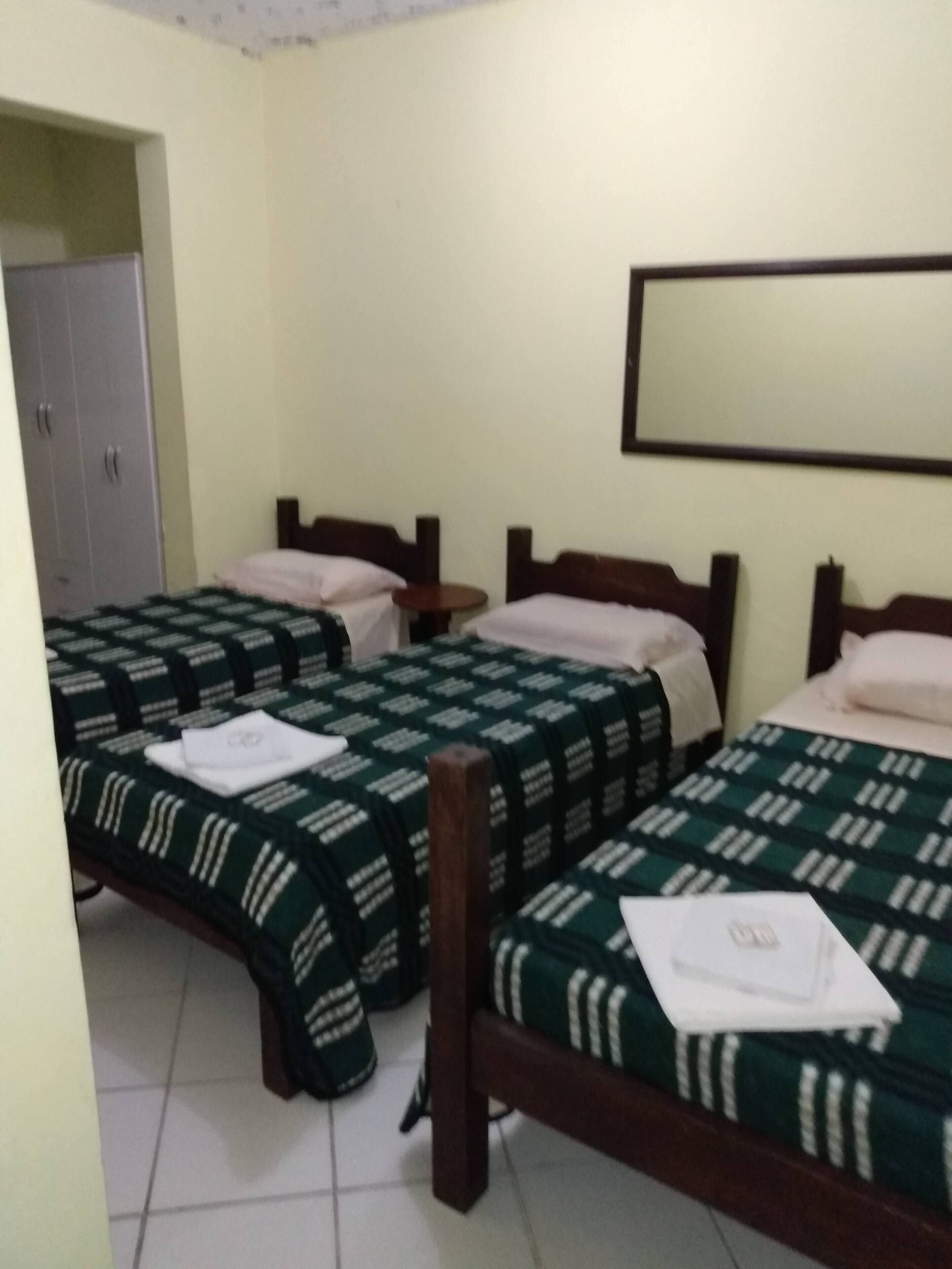 A hotel room with two single beds, a wardrobe, a small round table, and a mirror on the wall.
