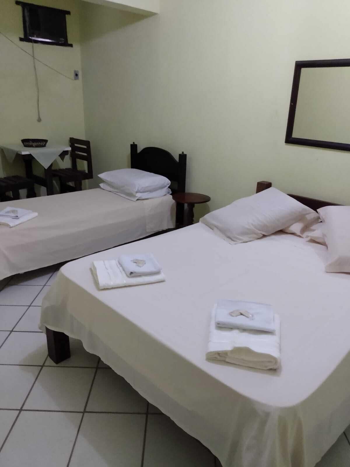 Quarto de hotel com duas camas, uma mesinha e uma cadeira.