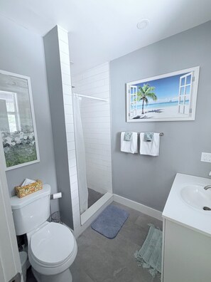 A bathroom with a toilet, shower, sink, and a wall-mounted towel rack. - Cozy spot next to Duval with swim spa - 2bed/2bath (Key West)