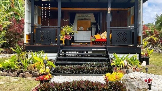A modern house with a covered porch, a kitchen visible through the open door, and a well-maintained garden with various plants and rocks. - Are Mii , a stylish one room container home (Arorangi District)