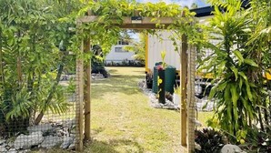 A garden with a wooden pergola, a pathway, and a fenced area with plants and rocks. - Are Mii , a stylish one room container home (Arorangi District)