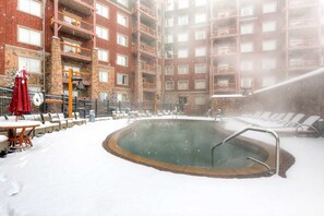 Zona de piscina exterior cubierta de nieve, con sillones reclinables y un jacuzzi.