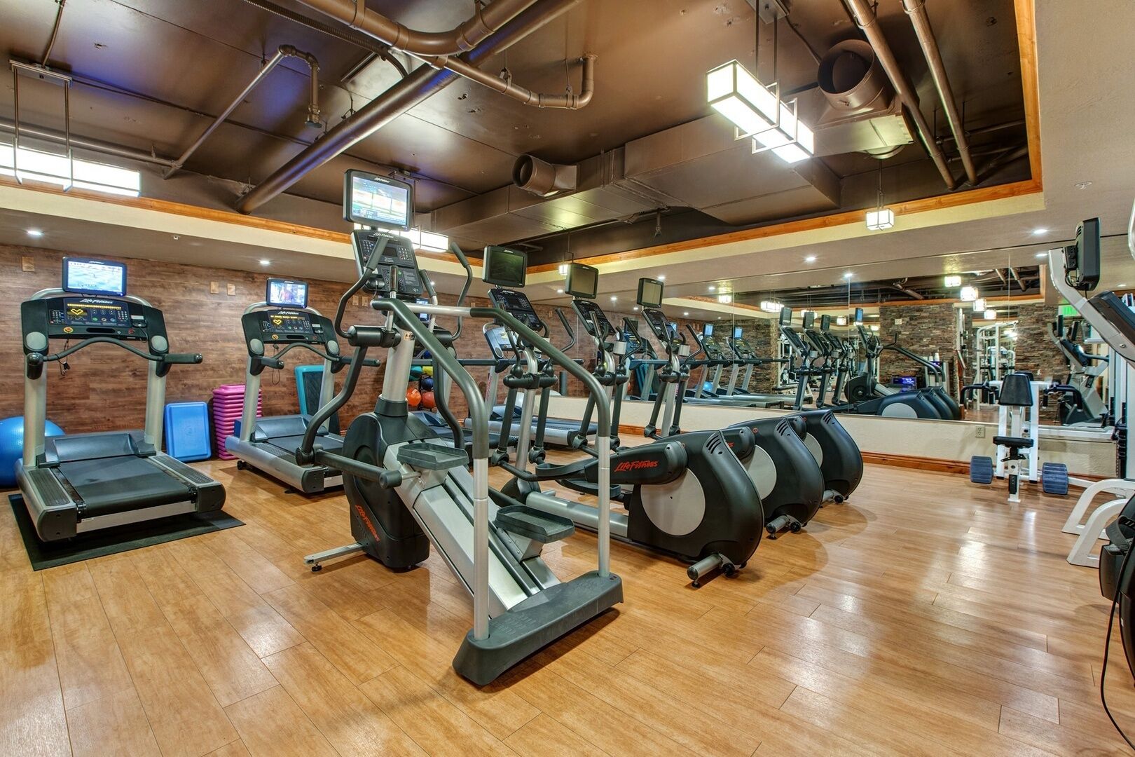 Ein Fitnessstudio mit mehreren Laufbändern, Crosstrainern und Ergometer, ausgestattet mit digitalen Bildschirmen und Spiegeln.