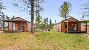 Two wooden cabins with outdoor seating, a covered patio, and a central communal area with a table and chairs.