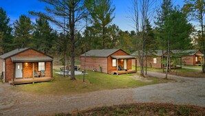 A row of log cabins with wooden decks, surrounded by trees.