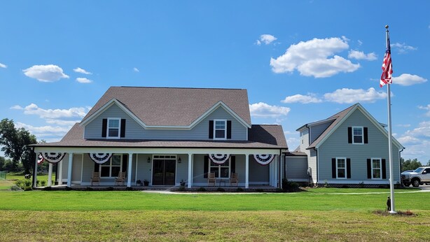 Ein zweistöckiges Haus mit Veranda, Fahnenmast und amerikanischer Flagge sowie einem Rasen.