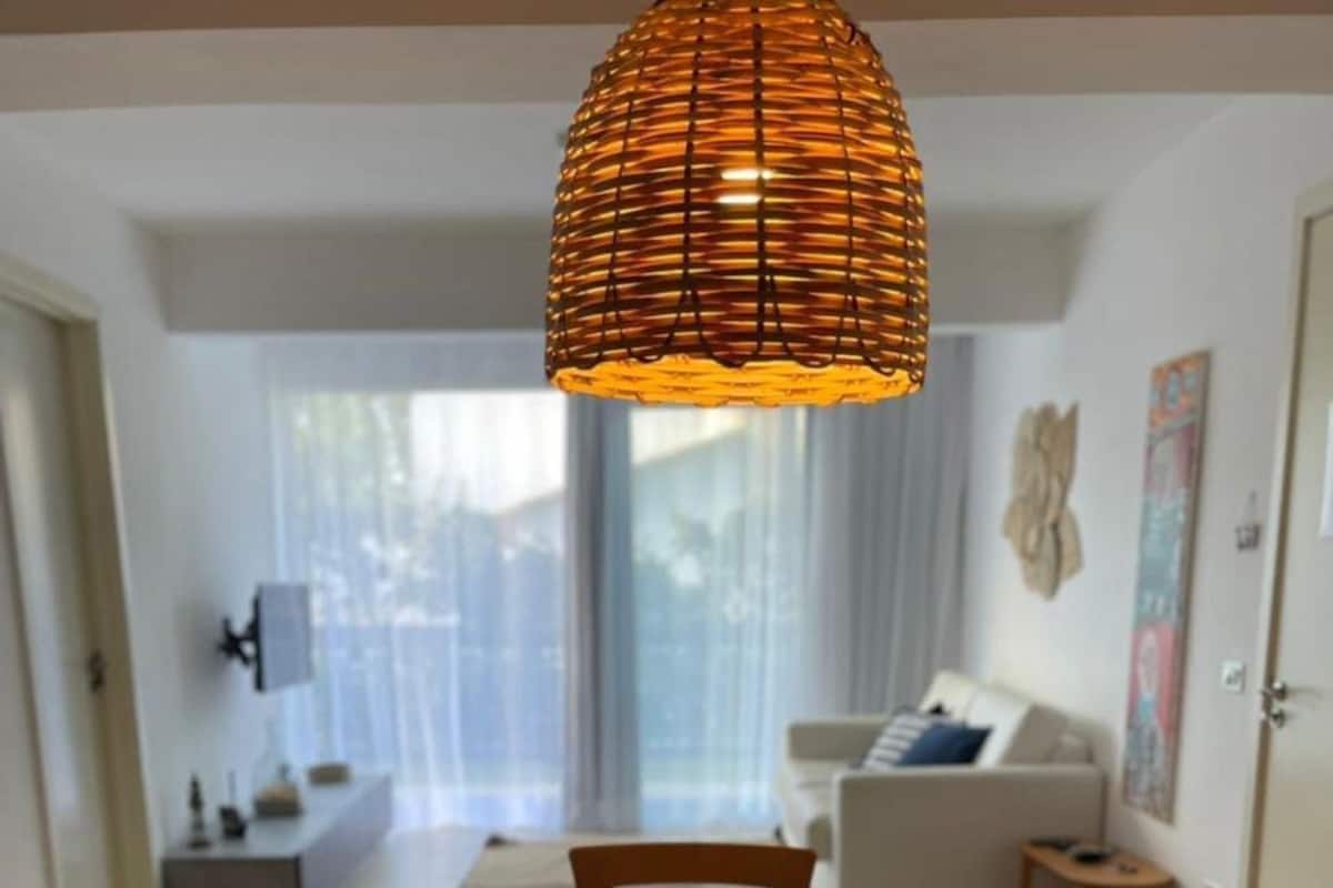 Comedor con una mesa redonda, cuatro sillas, una lámpara colgante tejida y una cesta con frutas sobre la mesa.