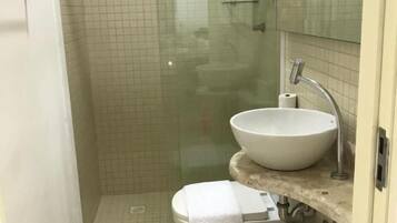 Um banheiro com chuveiro em gabinete de vidro, pia branca e vaso sanitário.