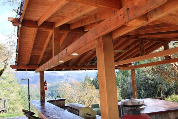Una pérgola de madera con encimera de piedra, una parrilla al aire libre y un extintor.