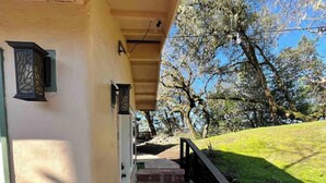 Un espace extérieur abrité, doté d’un chemin en briques menant à une porte, et entouré d’arbres et d’une pente herbeuse.